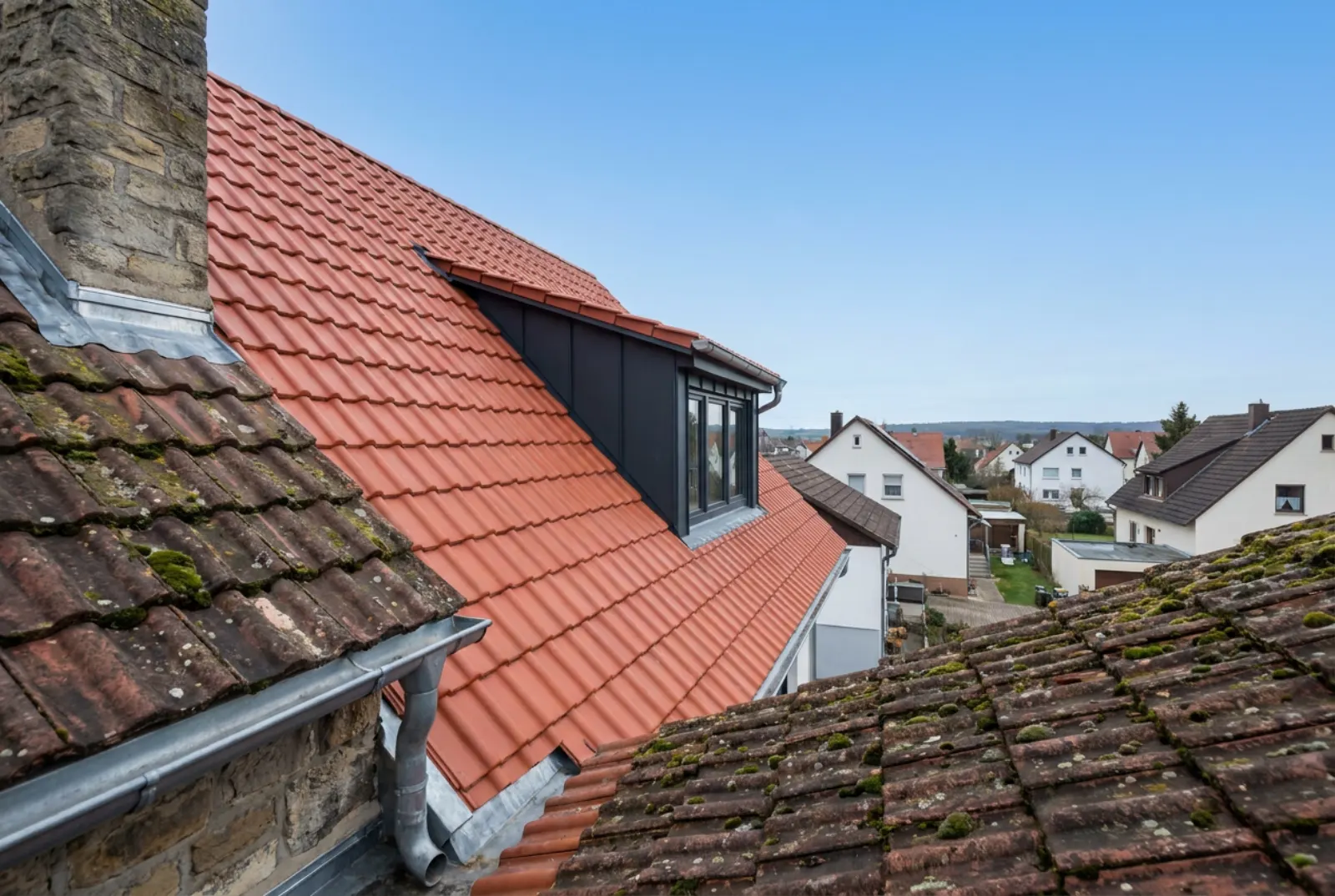 Steildach eines Einfamilienhauses mit neuen roten Tonziegeln und neuer Gaube vor blauem Himmel