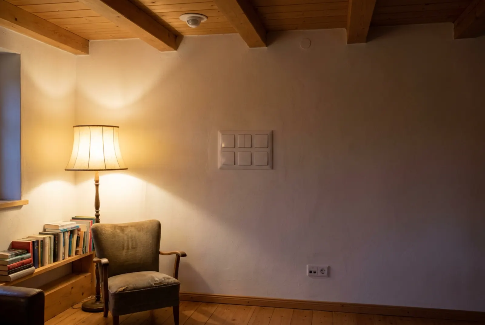 Wohnzimmerwand mit mehrfachem Schalterfeld, rundem Sensor an der Decke und Netzwerkdose im Abendlicht
