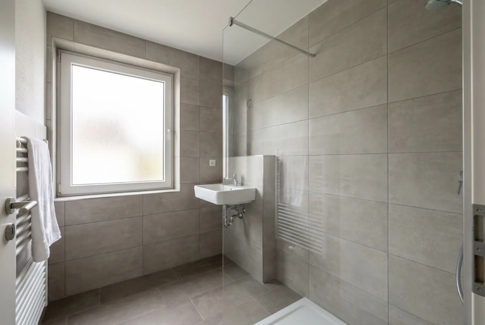 Neu gefliestes kleines Bad mit großen graubeigen Wand- und Bodenfliesen, Dusche mit Glaswand und Waschbecken