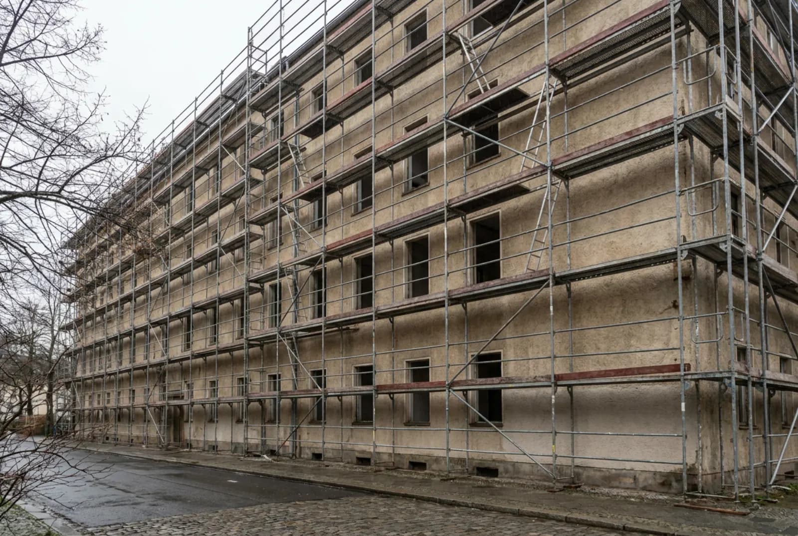 Vollständig aufgebautes Fassadengerüst mit Belägen, Bordbrettern und Geländern an einem verputzten Mehrfamilienhaus