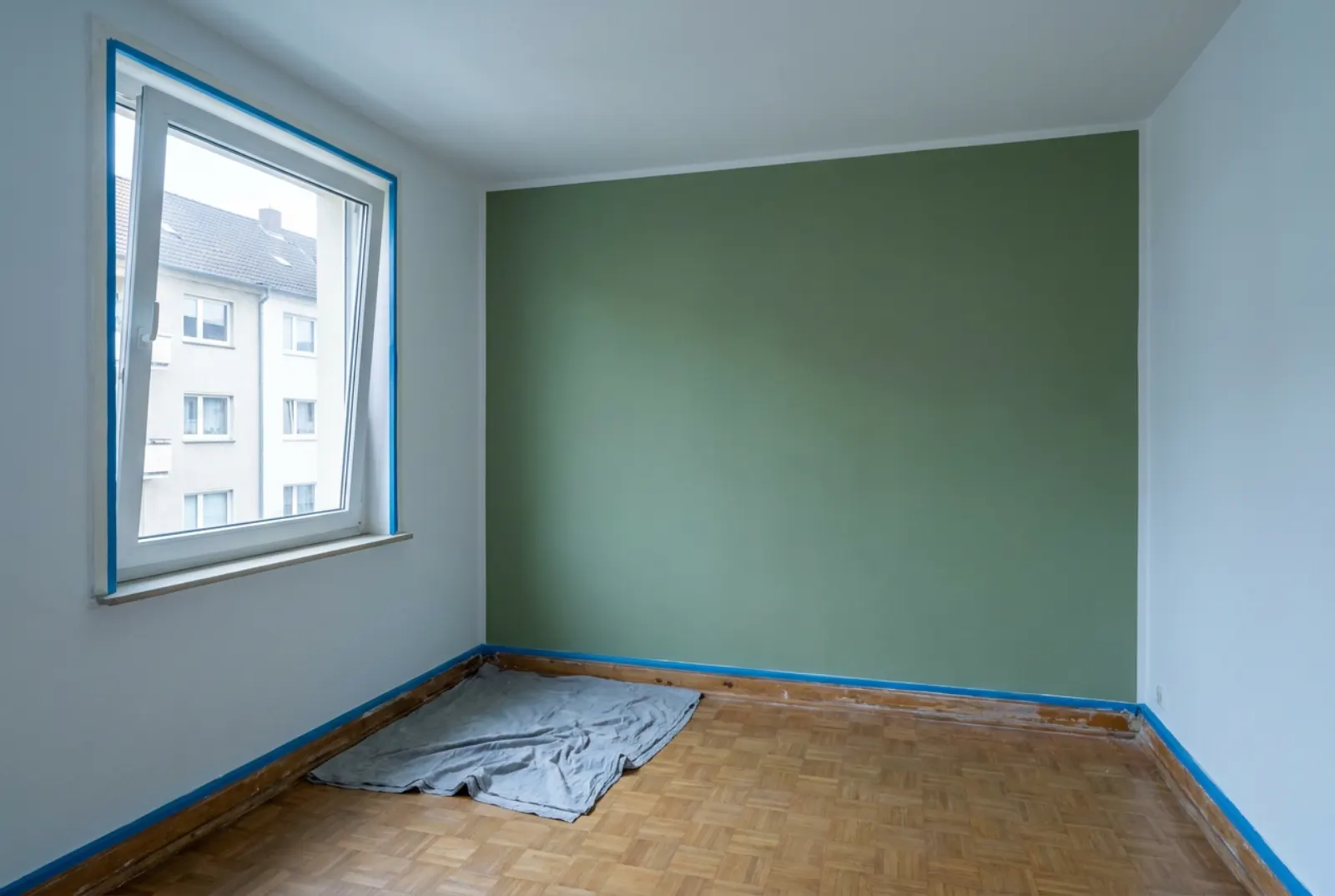 Leeres Wohnzimmer mit frisch gestrichenen weißen Wänden und einer gedeckt grünen Wand, Malerkrepp noch an der Sockelleiste
