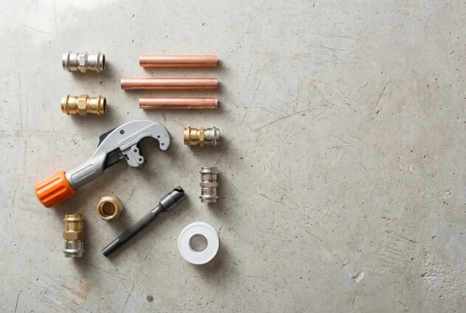 Kupferrohre, Pressfittings, Rohrabschneider mit orangem Griff und Teflonband auf einer Betonwerkbank